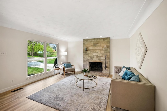 living room featuring wood finished floors, baseboards, a stone fireplace, and visible vents
