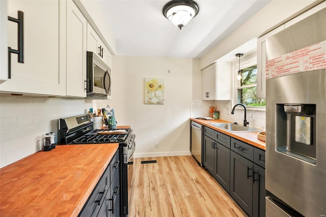 kitchen featuring white cabinets, a sink, stainless steel appliances, butcher block countertops, and decorative backsplash