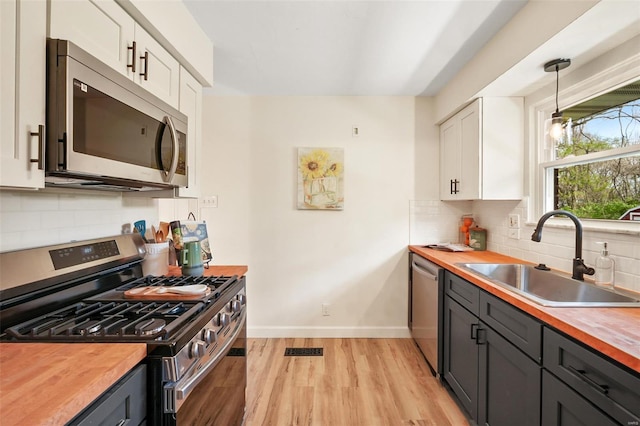 kitchen featuring light wood-style flooring, white cabinets, appliances with stainless steel finishes, a sink, and wooden counters