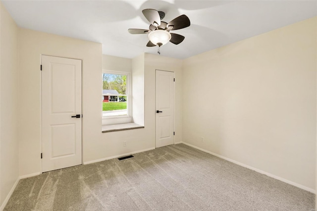 carpeted spare room featuring visible vents, baseboards, and ceiling fan