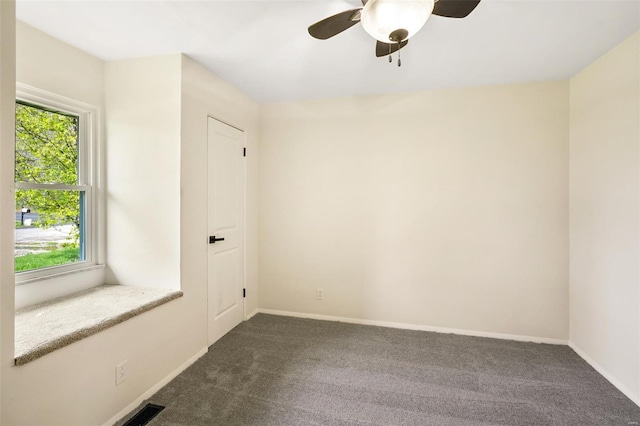 spare room featuring dark carpet, visible vents, and plenty of natural light