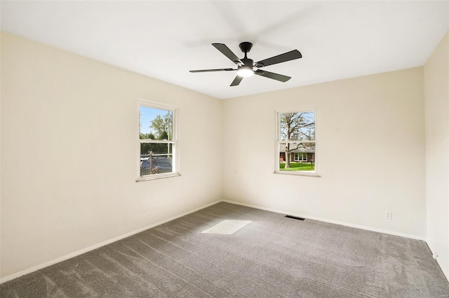 carpeted spare room featuring a wealth of natural light, visible vents, baseboards, and a ceiling fan