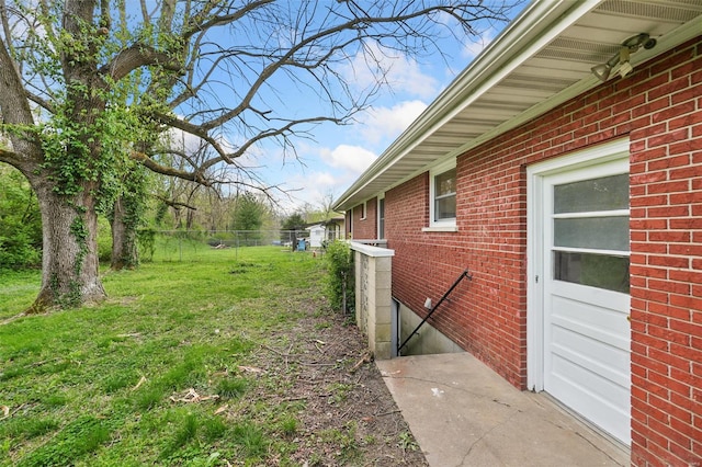 view of side of home featuring a yard, fence, and brick siding
