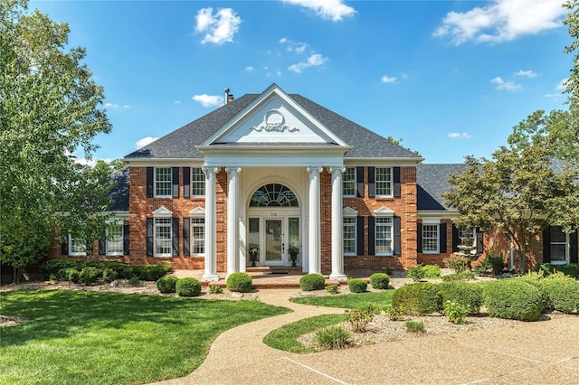 view of front of property featuring brick siding, roof with shingles, french doors, and a front yard