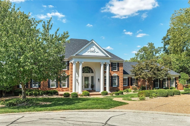 neoclassical home featuring brick siding, french doors, and a front yard