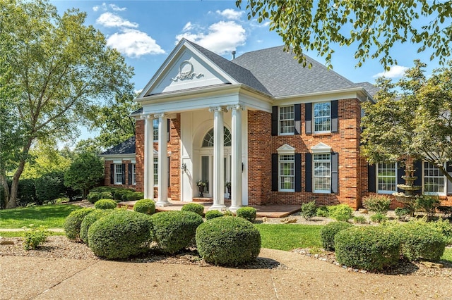 greek revival house with a porch, brick siding, and roof with shingles