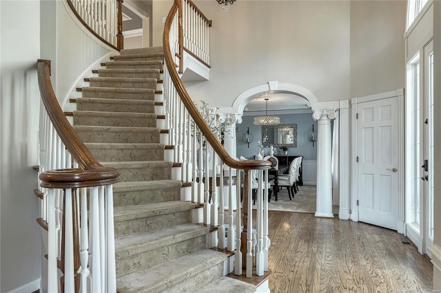 entryway with stairs, wood finished floors, a high ceiling, arched walkways, and a notable chandelier