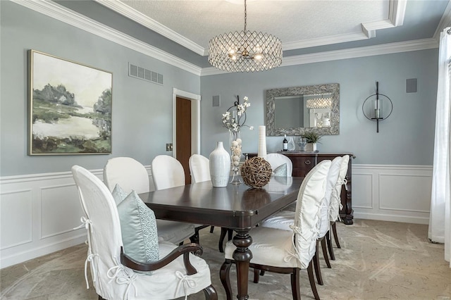 dining space with visible vents, crown molding, a wainscoted wall, an inviting chandelier, and a decorative wall