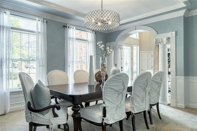 dining space featuring crown molding, arched walkways, a chandelier, and ornate columns
