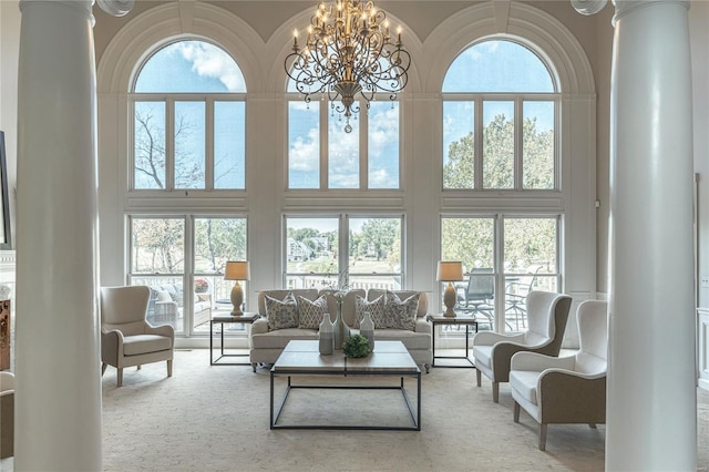 living area with a wealth of natural light, ornate columns, a chandelier, and a towering ceiling