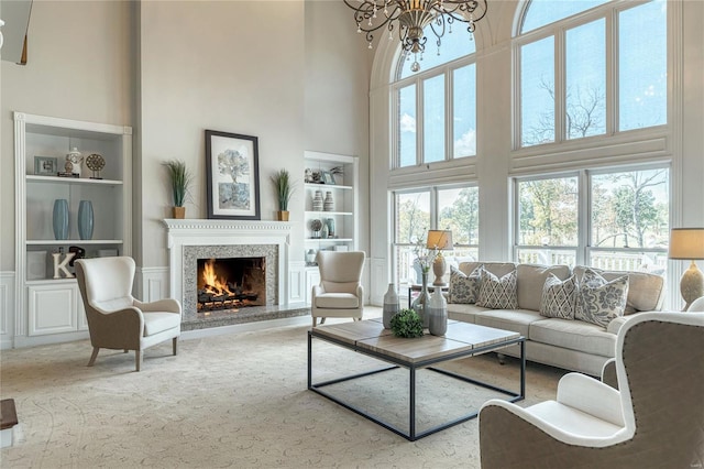 living area featuring a high ceiling, a warm lit fireplace, and built in shelves