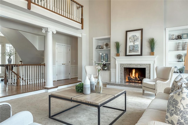 living area with built in features, a high ceiling, a fireplace, and decorative columns