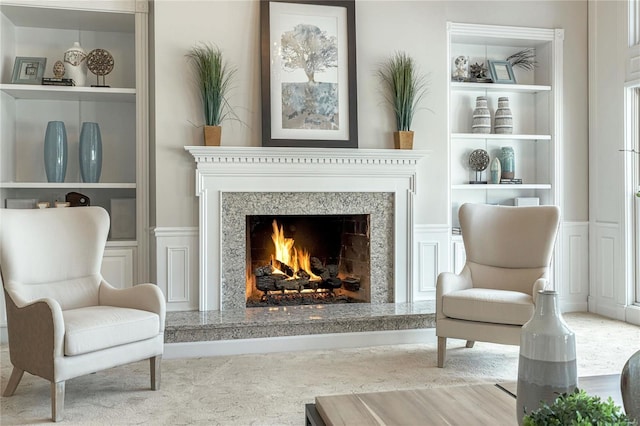 sitting room with a decorative wall, built in features, a wainscoted wall, and a fireplace