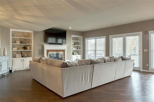 living area featuring baseboards, built in features, dark wood-type flooring, and a fireplace
