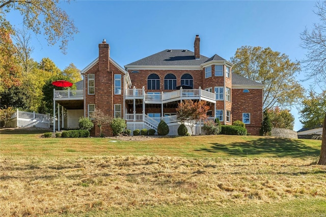 rear view of property featuring a lawn, a chimney, a balcony, and brick siding