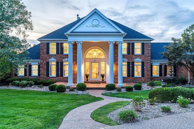 greek revival house with brick siding, roof with shingles, and a front yard