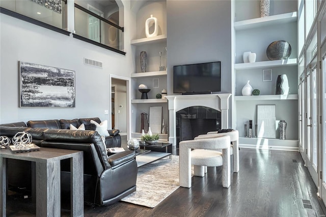 living room featuring visible vents, built in features, a high ceiling, and dark wood-style floors