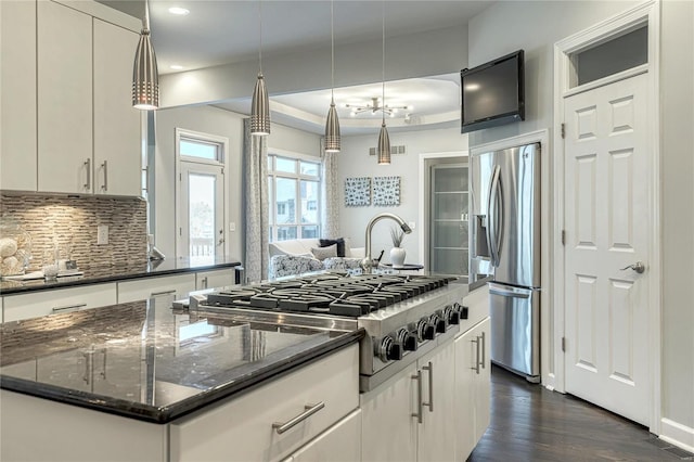 kitchen featuring decorative backsplash, appliances with stainless steel finishes, a center island, dark wood-style floors, and dark stone countertops