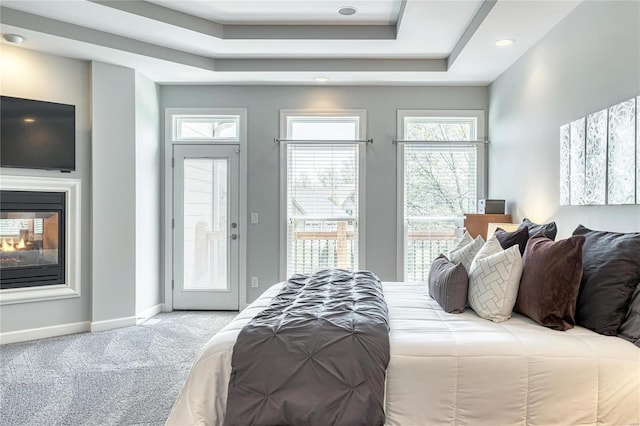carpeted bedroom with access to exterior, baseboards, recessed lighting, a tray ceiling, and a multi sided fireplace