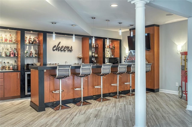 bar featuring ornate columns, wet bar, hanging light fixtures, and light wood-style floors
