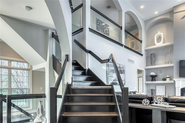stairway with a high ceiling, visible vents, built in features, and plenty of natural light