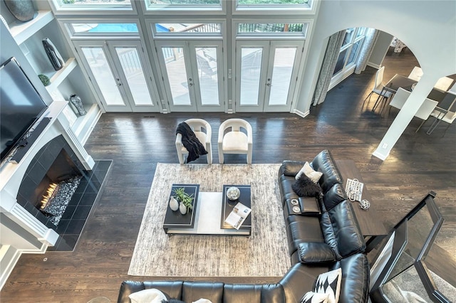 living room with arched walkways, a tiled fireplace, french doors, and wood finished floors
