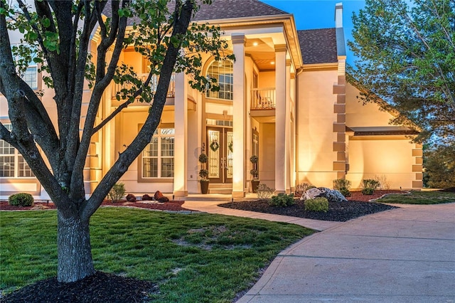 view of front of house with a shingled roof, a front lawn, stucco siding, and a balcony