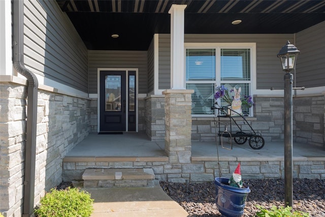 view of exterior entry featuring stone siding and covered porch