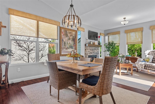 dining space featuring a chandelier, a fireplace, vaulted ceiling, baseboards, and wood finished floors