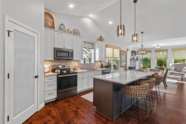kitchen with a sink, a kitchen bar, white cabinetry, appliances with stainless steel finishes, and plenty of natural light