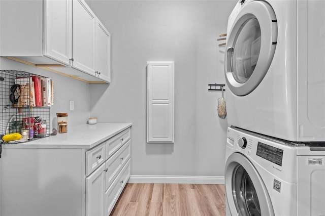 laundry room featuring stacked washing maching and dryer, light wood finished floors, cabinet space, and baseboards