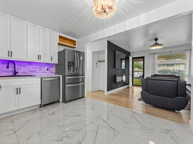 kitchen featuring marble finish floor, stainless steel appliances, white cabinetry, a sink, and a notable chandelier