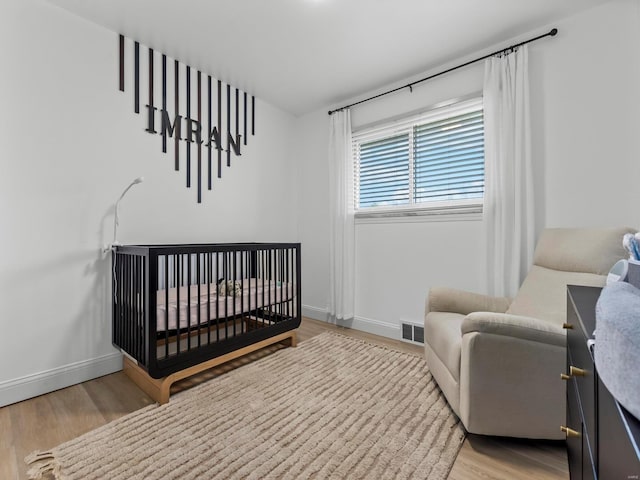 bedroom with a nursery area, baseboards, visible vents, and light wood-type flooring