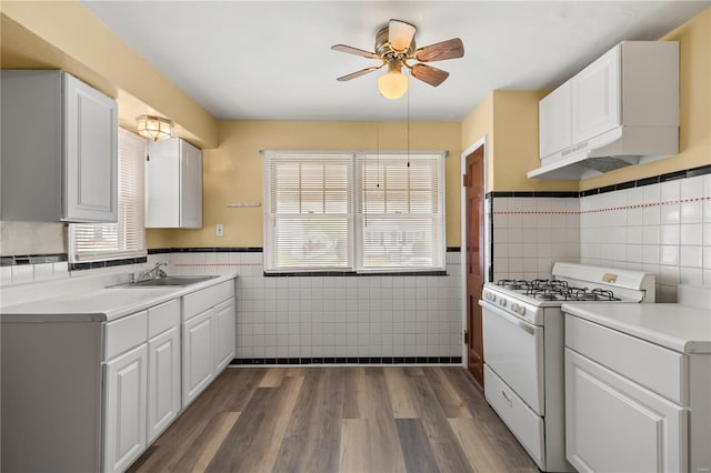 kitchen featuring wainscoting, tile walls, gas range gas stove, a ceiling fan, and dark wood finished floors