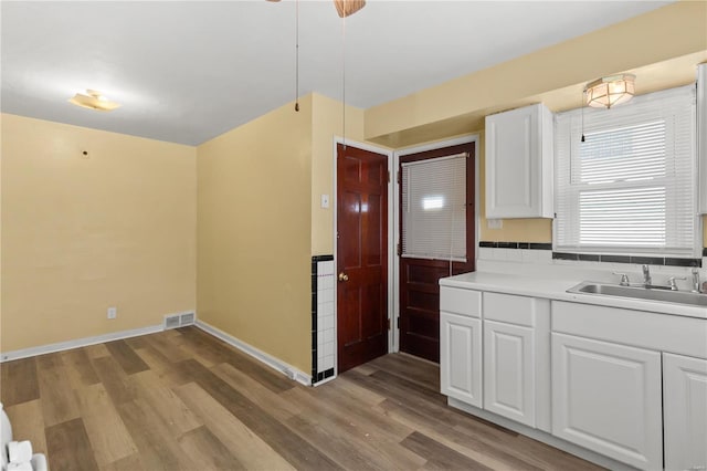 kitchen featuring white cabinets, a sink, light wood finished floors, baseboards, and visible vents