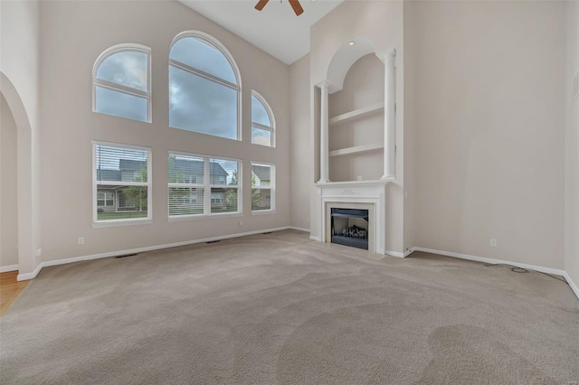 unfurnished living room with ceiling fan, baseboards, arched walkways, carpet floors, and a fireplace