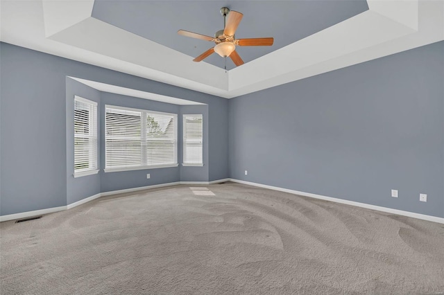 carpeted empty room featuring baseboards, visible vents, ceiling fan, and a tray ceiling