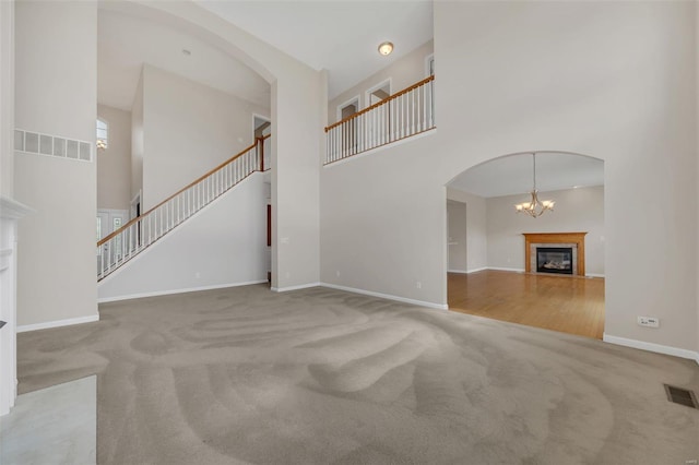 unfurnished living room with a high ceiling, carpet flooring, a glass covered fireplace, stairs, and visible vents
