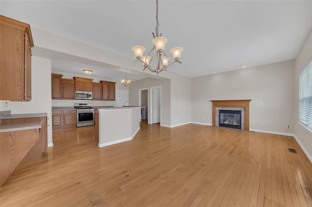 unfurnished living room with visible vents, an inviting chandelier, baseboards, light wood-type flooring, and a fireplace with flush hearth