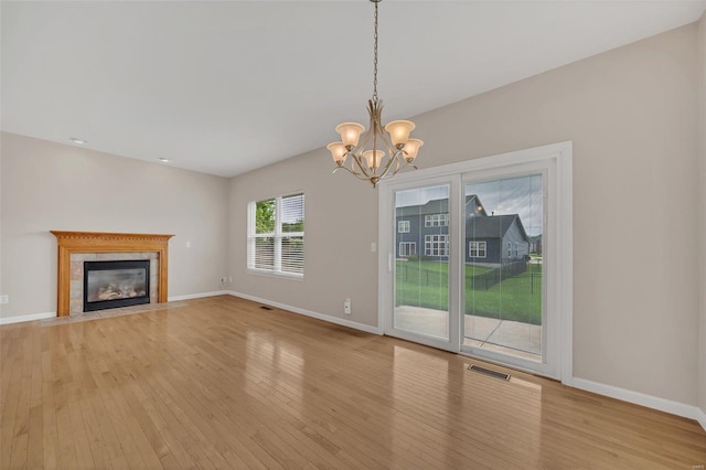 unfurnished living room featuring an inviting chandelier, a fireplace with flush hearth, light wood-style flooring, and baseboards