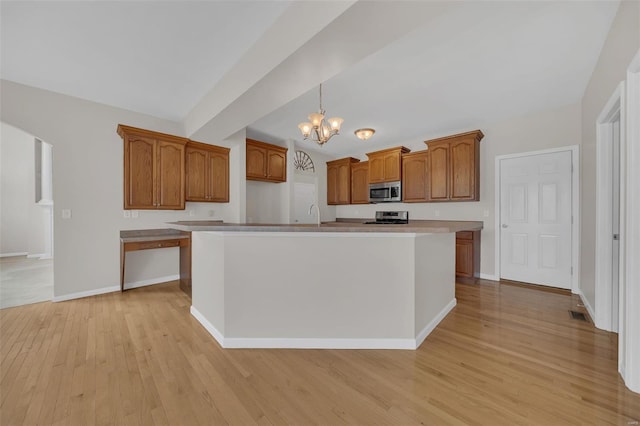 kitchen with an inviting chandelier, stainless steel appliances, brown cabinets, light wood finished floors, and a center island with sink