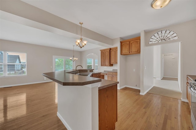 kitchen with light wood-style flooring, a chandelier, a spacious island, a sink, and baseboards