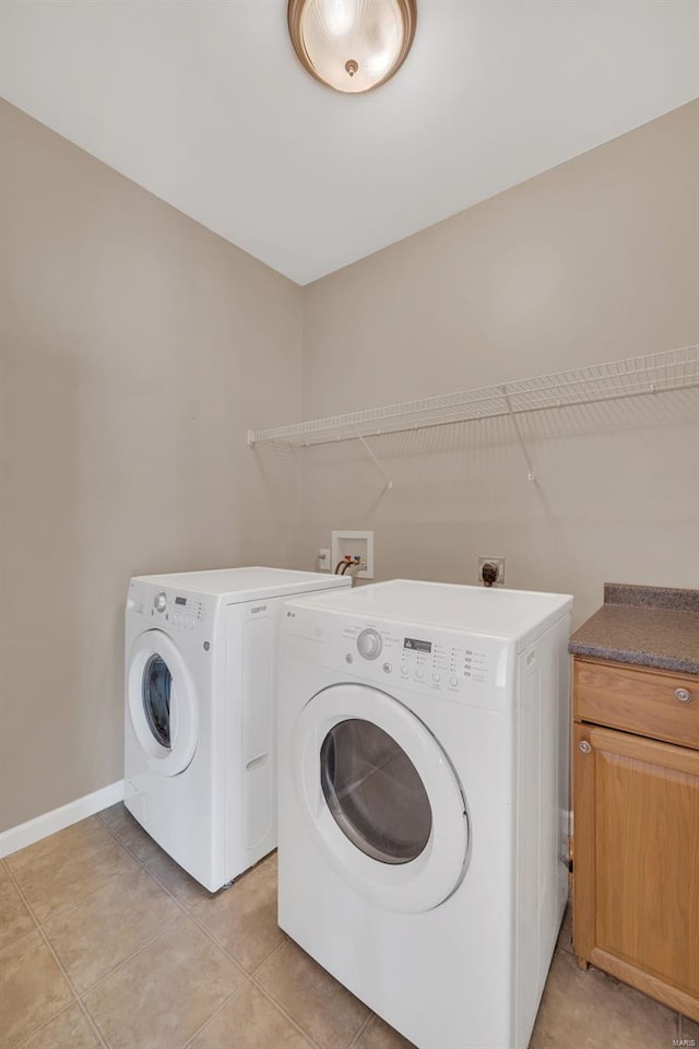 laundry area with light tile patterned floors, separate washer and dryer, cabinet space, and baseboards