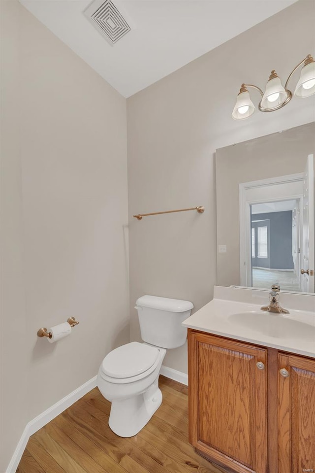 bathroom with vanity, toilet, visible vents, baseboards, and wood finished floors