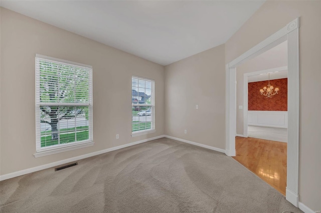 carpeted empty room featuring a notable chandelier, baseboards, and visible vents