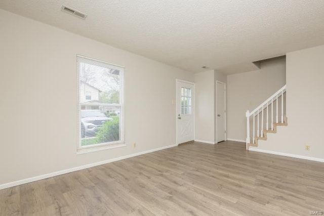 spare room with light wood-style floors, stairway, visible vents, and a textured ceiling