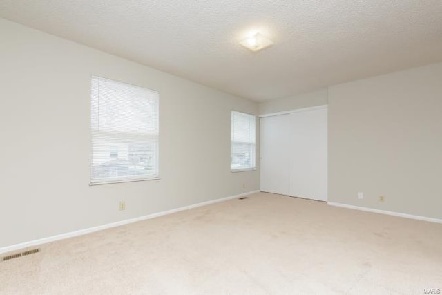 unfurnished room with baseboards, a textured ceiling, and light colored carpet