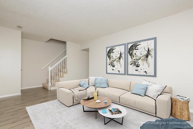 living area with wood finished floors, a textured ceiling, baseboards, and stairway