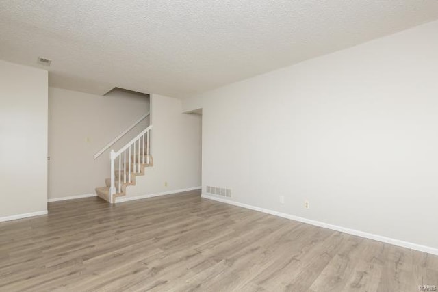 spare room with baseboards, light wood-style flooring, a textured ceiling, and stairs