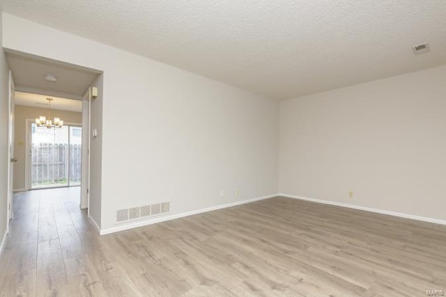 empty room featuring baseboards, a notable chandelier, wood finished floors, and visible vents